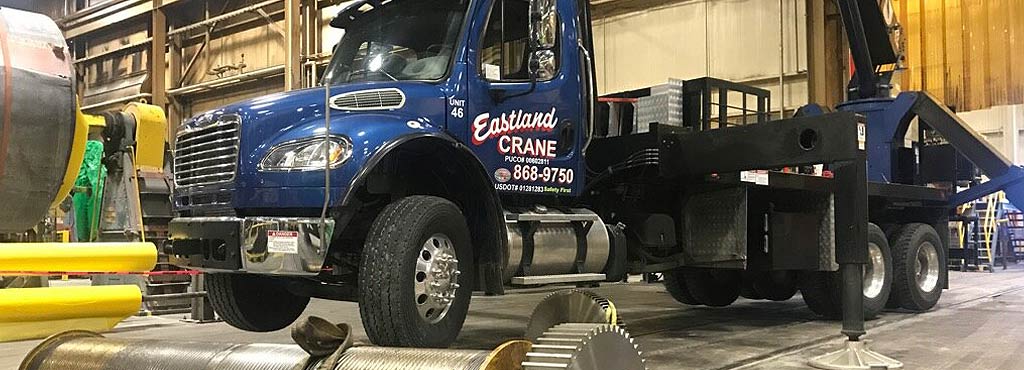 Eastland Crane boom truck lifting heavy equipment inside an industrial facility.